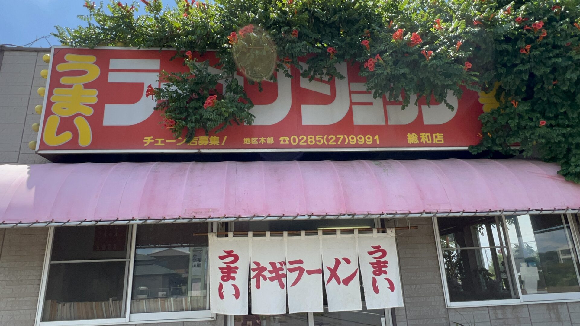 ラーメンショップ総和店を覆うノウゼンカズラの花に覆われる看板
